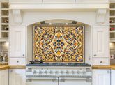 May include: A white kitchen with a stainless steel range hood and a stovetop. The range hood has a decorative tile backsplash with a floral pattern in shades of blue, yellow, and orange.