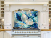 May include: A white kitchen with a glass stovetop backsplash featuring an abstract design of blue and white leaves. The backsplash is installed above a stainless steel stove with a black burner grate.