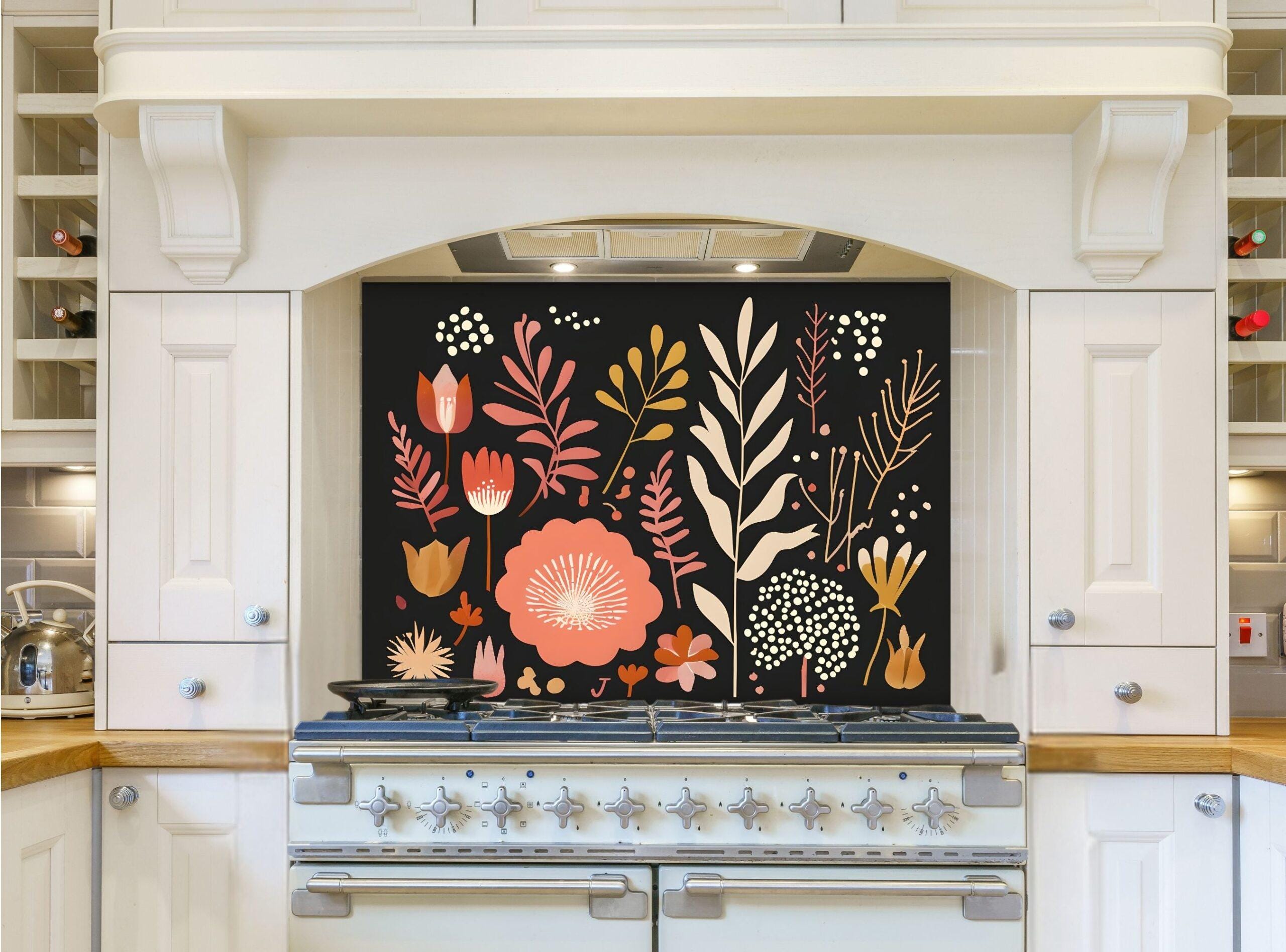 May include: A white kitchen with a black range hood and a floral patterned backsplash. The backsplash features a variety of flowers and leaves in shades of pink, orange, and yellow on a black background. The range hood is above a white range with six burners and a black oven door.