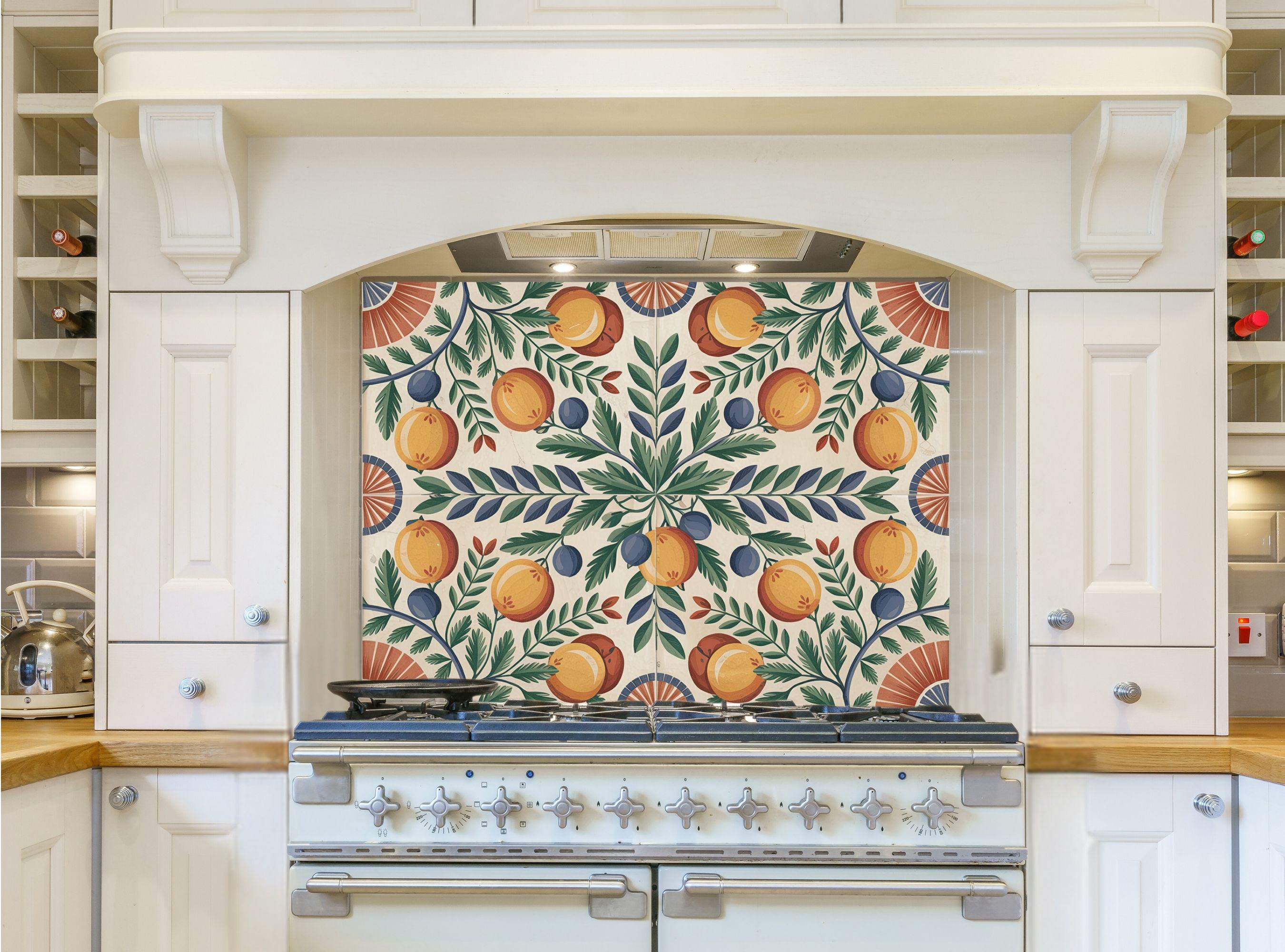 May include: A white kitchen with a range hood and a stove. The range hood has a decorative backsplash with a pattern of green leaves, orange and yellow fruit, and blue berries. The stove is silver with black knobs and a black top.
