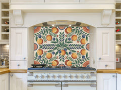 May include: A white kitchen with a range hood and a stove. The range hood has a decorative backsplash with a pattern of green leaves, orange and yellow fruit, and blue berries. The stove is silver with black knobs and a black top.