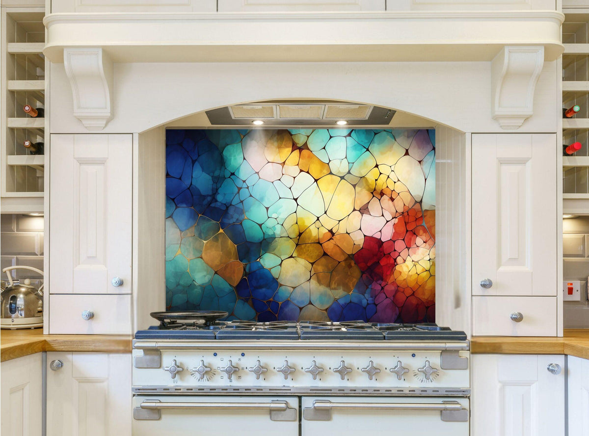 May include: A white kitchen range with a colorful abstract backsplash. The backsplash is made of glass tiles in shades of blue, green, yellow, orange, and red. The range has a black burner grate and a white control panel with silver knobs.