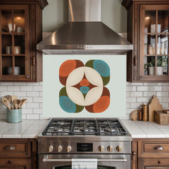 May include: A kitchen backsplash with a retro-style geometric design. The design features a central white circle with a starburst pattern, surrounded by orange, teal, and brown rounded shapes. The backsplash is mounted above a stainless steel gas range.